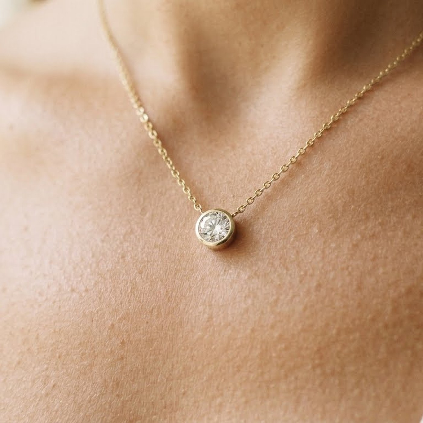 A bezel-set diamond pendant on a fine gold chain, worn at the collarbone